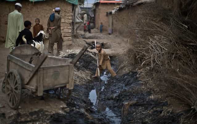 An Afghan refugee boy, center, uses a shovel to clear a sewage path outside his home in a poor neighborhood on the outskirts of Islamabad, Pakistan, Thursday, September 26, 2013. Pakistan hosts over 1.6 million registered Afghans, the largest and most protracted refugee population in the world, according to the U.N. refugee agency, thousands of them still live without electricity, running water and other basic services. (Photo by Muhammed Muheisen/AP Photo)