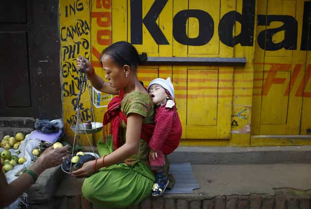 A child sleeps on the back of her mother as she sells fruits to customers along the streets in the ancient city of Bhaktapur, near Nepal's capital Kathmandu September 23, 2013. (Photo by Navesh Chitrakar/Reuters)