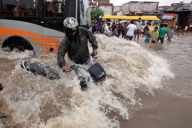 An Indian motorist tries to balance himself as a bus drives past him on a flooded road after heavy rains in Ahmadabad, India, Wednesday, September 25, 2013. Massive flooding has forced 15,000 people to evacuate villages in the west Indian state of Gujarat where heavy rains and swollen rivers have inundated cities and closed off roads and railway lines. (Photo by Ajit Solanki/AP Photo)