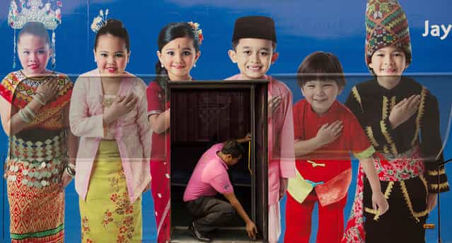A man (C) opens a bus door through within a poster showing the Malaysia ethnic communities with traditional dress in Kuala Lumpur on September 25, 2013. The Malaysian government's new measures to benefit the Malay majority are angering the multi-ethnic nation's other races and raising fears they could accelerate a [brain drain] of talent heading overseas. (Photo by Mohd Rasfan/AFP Photo)