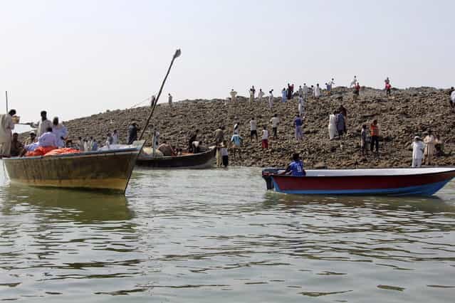 People use boats as they visit an island that rose from the sea following an earthquake, off Pakistan's Gwadar coastline in the Arabian Sea September 25, 2013. A major earthquake hit a remote part of western Pakistan on Tuesday, killing at least 45 people and prompting the new island to rise from the sea just off the country's southern coast. The earthquake was so powerful that it caused the seabed to rise and create a small, mountain-like island about 600 meters off Pakistan's Gwadar coastline. Television channels showed images of a stretch of rocky terrain rising above the sea level, with a crowd of bewildered people gathering on the shore to witness the rare phenomenon. (Photo by Reuters/Stringer)