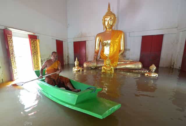 A buddhist monk paddles boat past a buddha statue at a temple in Ayutthaya province, north of Bangkok on October 3, 2013. The Disaster Prevention and Mitigation Department reported that 25 provinces in Thailand are still flooded and 27 people have died idue to the flood. (Photo by Pornchai Kittiwongsakul/AFP Photo)