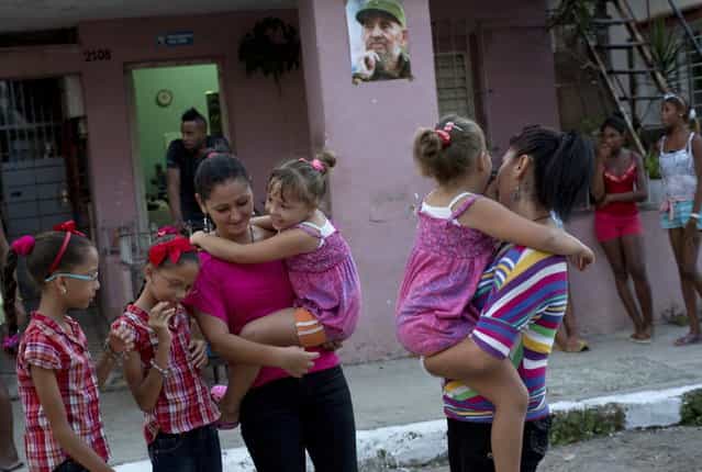 In this September 23, 2013 photo, from left to right, nine-year-old twins Camila and Carla Rodriguez, and 18-year-old twins Kamar and Sahar Youssef holding six-year-old twins Asley and Aslen Velazquez, pose for portraits along their street where a poster of Fidel Castro hangs in Havana, Cuba. The twins are just some of the 12 sets of twins living along two consecutive blocks in western Havana. (Photo by Ramon Espinosa/AP Photo)