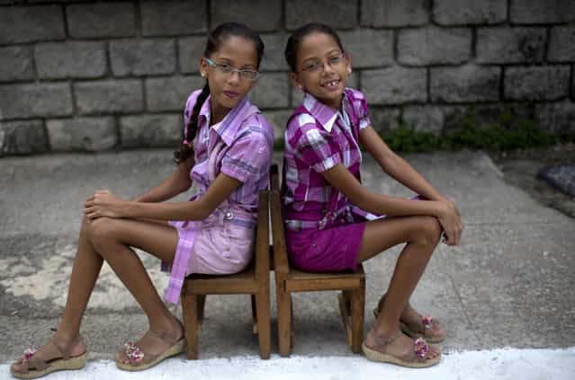 In this September 29, 2013 photo, nine-year-old twin sisters Camila, left, and Carla Rodriguez pose for a portrait along their street in Havana, Cuba. 12 sets of twins live along two consecutive blocks in western Havana, ranging in age from newborns to senior citizens. [We love living on this block because we have twin friends], said Carla. (Photo by Ramon Espinosa/AP Photo)