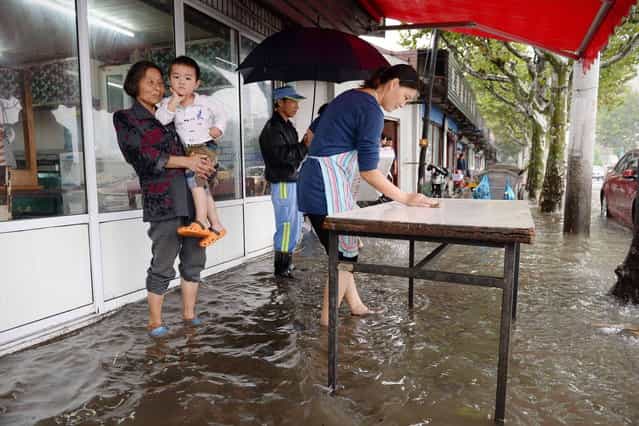 A woman (R) cleans a table on a flooded street in Shanghai after typhoon Fitow brought heavy rain to the area on October 8, 2013. Typhoon Fitow, which barrelled into China's east coast early on October 7 packing winds of more than 200 kilometres (124 miles) an hour, killed at least five people and impacted 4.5 million, state media reported. (Photo by AFP Photo)