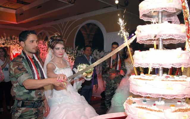 Photo released by the news agency of the Syrian government shows a soldier forces of Bashar al-Assad cutting the wedding cake with a bride during mass ceremony in which several soldiers were married in Homs, on Oktober 10, 2013. (Photo by AFP Photo/Sana)
