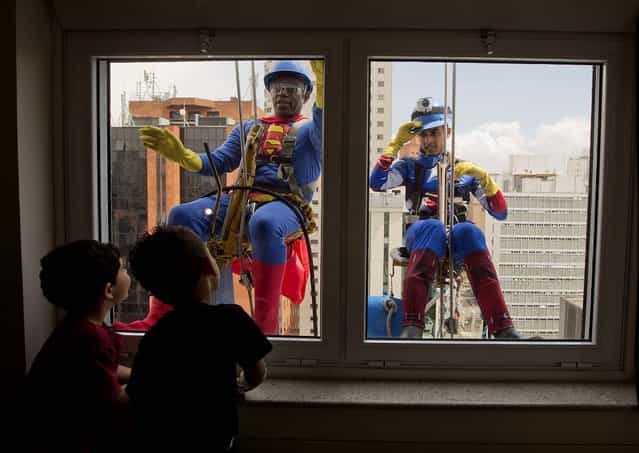 Young patients watch high rise window washers wearing Superman and Captain America costumes clean the windows of the Sabara Children's Hospital in Sao Paulo, Brazil, on Oktober 11, 2013. The hospital had their regular window washers dress up in super hero costumes to commemorate Children's Day. (Photo by Andre Penner/Associated Press)