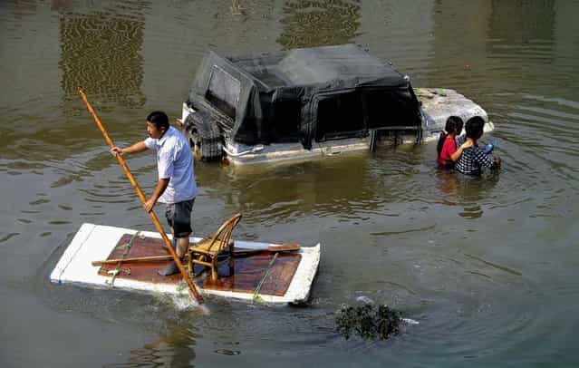 A man paddles a makeshift raft as residents walk past a partially submerged car on a flooded street in Yuyao, Zhejiang province, on Oktober 11, 2013. Power remains cut for the third consecutive day for tens of thousands of households in after Typhoon Fitow-triggered downpours lashed the city. (Photo by Lang Lang/Reuters)