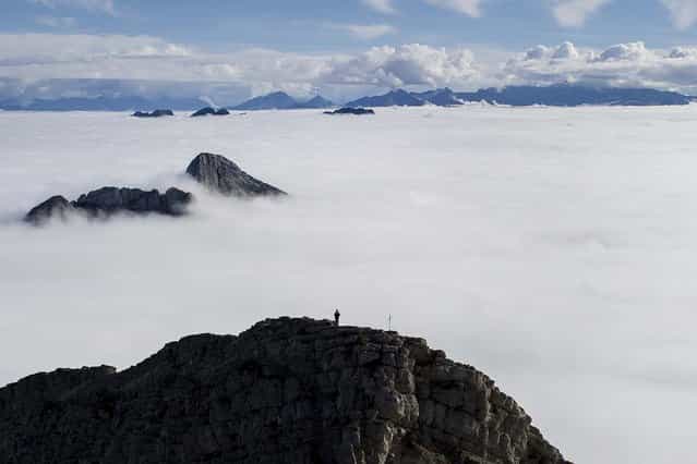 A man watches a sea of clouds as he stands on a side summit of Mount Saentis in Urnaesch, near Appenzell, Switzerland, on Oktober 8, 2013. (Photo by Gian Ehrenzeller/Keystone)