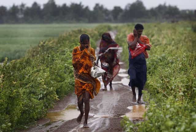 Indian villagers braving strong winds and rain reach for a cyclone center, in village Podampeta, in Ganjam district about 200 kilometers (125 miles) from the eastern Indian city Bhubaneswar, India, Saturday, October 12, 2013. Strong winds and heavy rains pounded India's eastern coastline Saturday, as hundreds of thousands of people took shelter from a massive, powerful Cyclone Phailin expected to reach land in a few hours. (Photo by Biswaranjan Rout/AP Photo)
