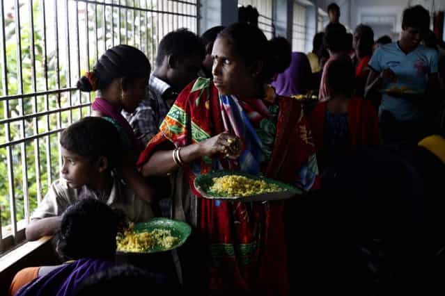 Evacuated Indian villagers watch strong winds and rain as they eat food in a temporary cyclone shelter in Chatrapur, in Ganjam district about 200 kilometers (125 miles) from the eastern Indian city Bhubaneswar, India, Saturday, October 12, 2013. Strong winds and heavy rains pounded India's eastern coastline Saturday, as hundreds of thousands of people took shelter from a massive, powerful Cyclone Phailin expected to reach land in a few hours. (Photo by Biswaranjan Rout/AP Photo)