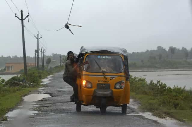 A man tries to avoid a broken electricity cable as he rides on an auto rickshaw to a safer place in Ichapuram town in Srikakulam district in the southern Indian state of Andhra Pradesh October 12, 2013. Rain and wind lashed India's east coast on Saturday, forcing more than 400,000 people to flee to storm shelters as one of the country's largest cyclones closed in, threatening to cut a wide swathe of devastation through farmland and fishing hamlets. Filling most of the Bay of Bengal, Cyclone Phailin was about 200 km (124 miles) offshore by noon on Saturday, satellite images showed, and was expected to hit land by nightfall. (Photo by Adnan Abidi/Reuters)