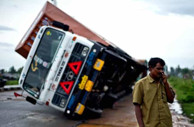 Indian truck driver Jairam Yadav speaks on his mobile phone after his truck carrying Toyota cars was overturned by strong wind on the National Highway linking Andhra Pradesh and Odisha on October 13, 2013. (Photo by AFP Photo/YAYANA)