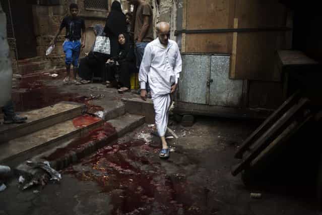 A man walks through an alley covered with bloodstained water on the first day of Eid al-Adha in Cairo, Egypt, Tuesday, October 15, 2013. Muslims worldwide are celebrating Eid al-Adha, or the Feast of the Sacrifice, by sacrificial killing of sheep, goats, cows or camels. The slaughter commemorates the biblical story of Abraham, who was on the verge of sacrificing his son to obey God's command, when God interceded by substituting a ram in the child's place. (Photo by Manu Brabo/AP Photo)