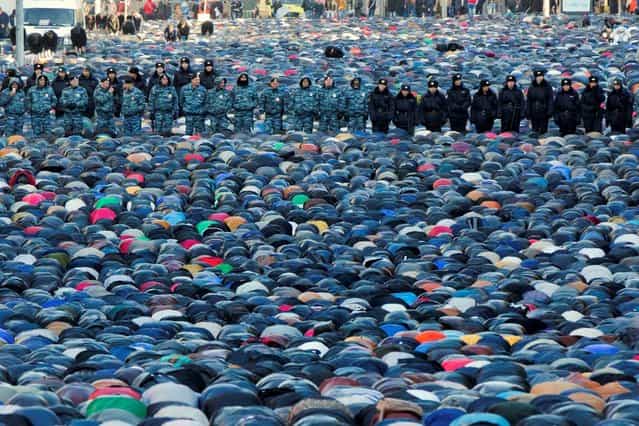 Russian police officers stand guard as Muslims pray outside the main Moscow mosque during celebrations of Eid al-Adha, a feast celebrated by Muslims worldwide, which Muslims in Russia call Kurban-Bairam in Moscow, Russia, Tuesday, October 15, 2013. According to the press service of Moscow's main police department, about four thousand police officers, Interior troops and others will be ensuring security during the Eid al-Adha celebration events. (Photo by Evgeny Feldman/AP Photo)