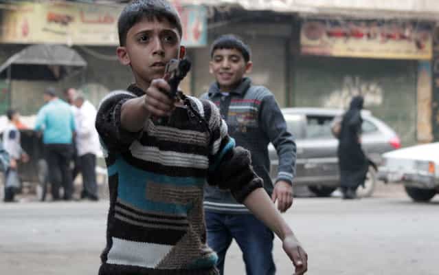 A child plays with a toy gun in the Bustan al-Qasr neighbourhood of the northern Syrian city of Aleppo on October 15, 2013. The United States said there was an [urgent] need to set a date for so-called Geneva 2 peace talks, despite a leading opposition group's rejection of the process. (Photo by Karam Al-Masri/AFP Photo)