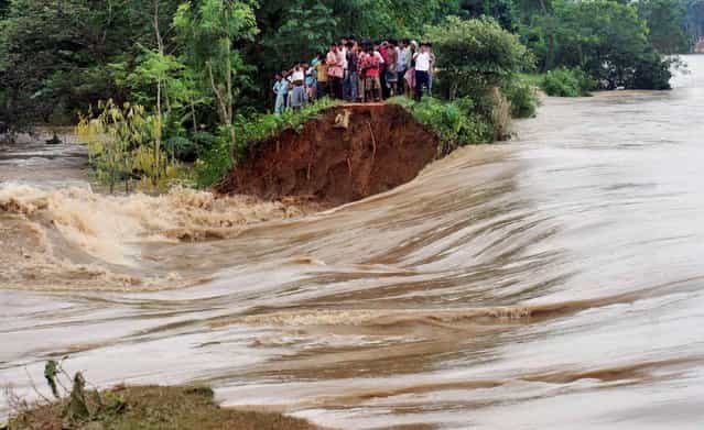 Indian villagers stand on the breached embankment of swollen Kangsabati river at Samat village in West Bengal state, India, Tuesday, October 15, 2013. Heavy torrential rain in the aftermath of weekend Cyclone Phailin have made rivers to overflow causing flood situation in the state. (Photo by AP Photo)