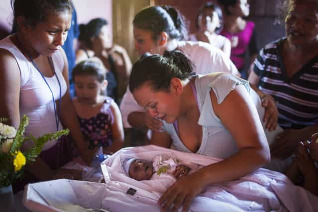 Valeria Michel Hercules lifts up her dead baby, Gabriel Alexander, at a funeral held in the Las Victorias district of San Salvador. It is unclear how he died. His mother, Valeria Michel Hercules, was in prison when she went into labour. The guards allegedly delayed her transfer to hospital despite her appeals. When she finally arrived, the infant was dead and she had to deliver a still born child the next day. (Photo by Adam Hinton)