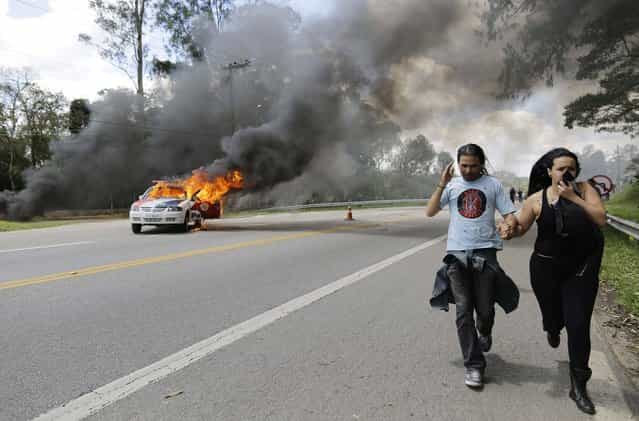 Demonstrators run away from the Instituto Royal laboratory to escape tear gas fired by police, as a police car burns along a road leading to the lab in Sao Roque, Brazil, Saturday, October 19, 2013. Clashes between animal rights activists and police outside the lab came one day after activists broke into the lab and released beagle dogs being used to test for adverse effects of drugs manufactured by the pharmaceutical industry. Protesters returned Saturday to see if there were more animals in the building. (Photo by Nelson Antoine/AP Photo)