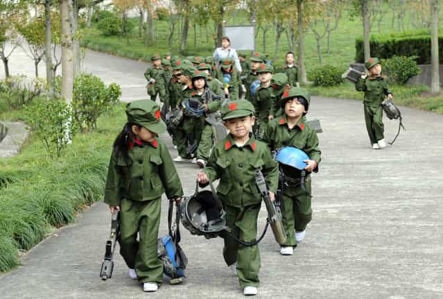 Kindergarten children dressed in military uniforms carry toy guns at a park in Dongyang, Zhejiang province, October 25, 2013. Students of different ages came to the park to experience Red Army culture and to receive patriotic education, according to local media. (Photo by Reuters/Stringer)