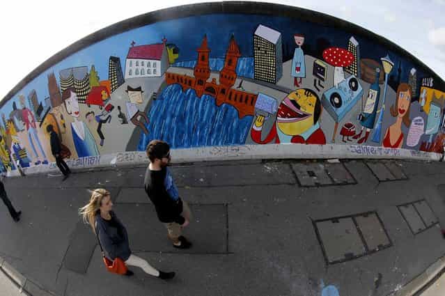 People walk past to the newly painted artwork of contemporary German Pop artist Jim Avignon at the open air 0.8-mile painted section of the Berlin Wall known as the [East Side Gallery] in Berlin, on Oktober 23, 2013. (Photo by Fabrizio Bensch/Reuters)