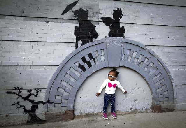 A child poses for a photo under the art piece by Banksy on October 17, 2013 before the metal gate was installed. (Photo by Carlo Allegri/Reuters)