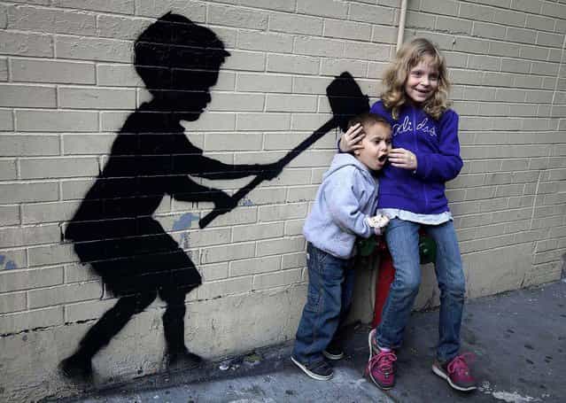 Children pose for their parent's photo with an installation of Banksy's art on October 20, 2013. (Photo by Carlo Allegri/Reuters)