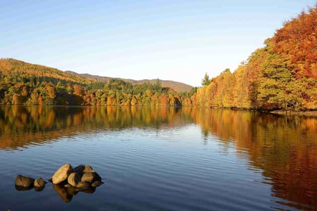 Autumn trees are reflected in the water of Loch Faskally. (Photo by Russell Cheyne)