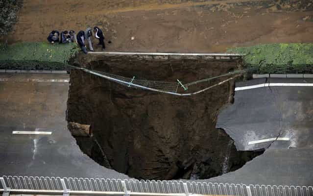 People look at a large sinkhole on a street after a water pipe broke underneath it in Xi'an, Shaanxi province, China, on October 27, 2013. (Photo by Reuters/Stringer)