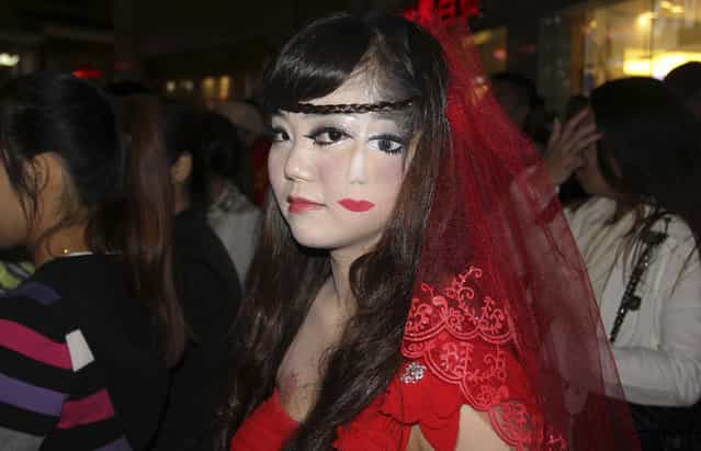 A woman who drew part of a face on her cheek, stands among the crowd at a costume party to celebrate Halloween in Wuhan, Hubei province October 31, 2013. (Photo by Reuters/China Daily)