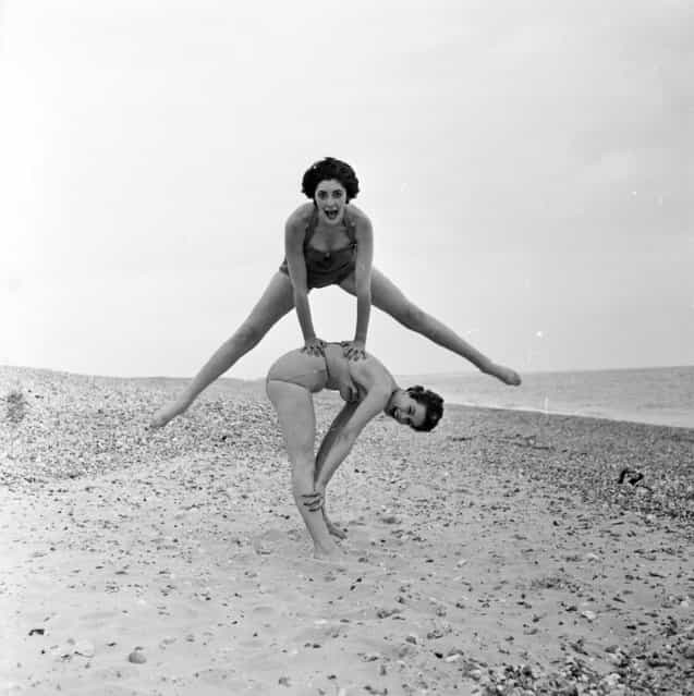 Fashion models Darien Leigh and Valerie Drew play leap-frog on the beach. 2nd July 1956. (Photo by Harry Kerr)