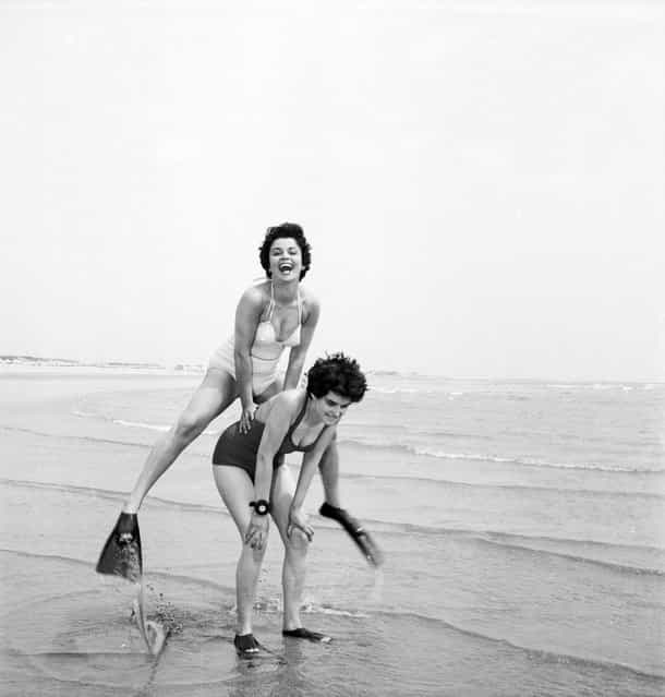 Two women wearing fins play leap-frog on the beach, 1955. (Photo by Peter Purdy)