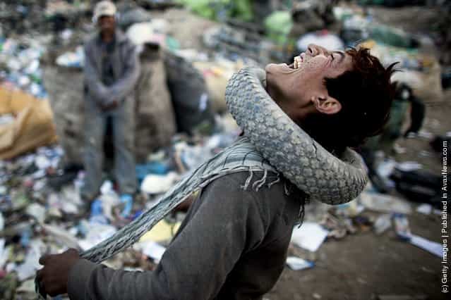 An Afghan man wears a tire around his neck while sorting through plastic and metal items near a rubbish dump