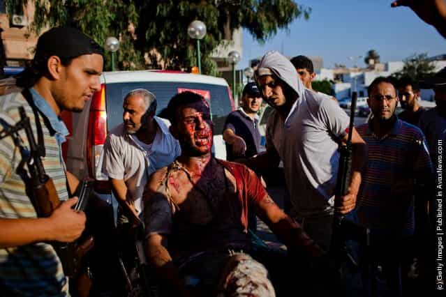 Libyan rebel fighters protect a pro-Gaddafi loyalist fighter from angry onlookers as he is brought in for medical attention to the Tripoli Central Hospital