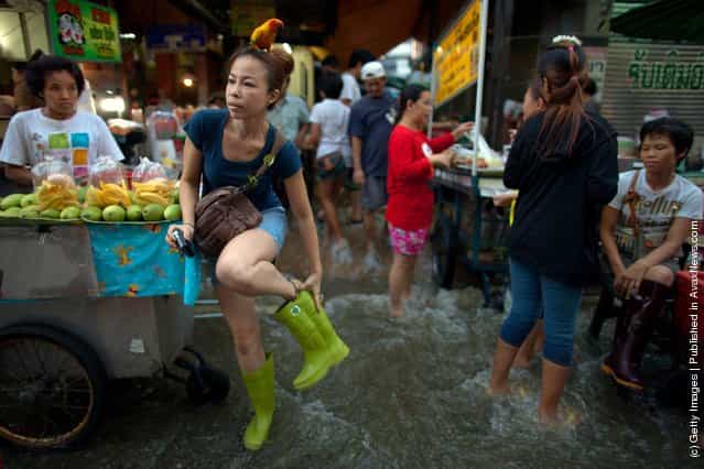 Patarawan fixes her boots as her parrot, Sim sits on her head as she goes shopping for dinner at a busy flooded market near the Chao Phraya river