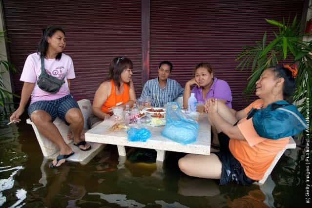Thai women eat and drink whiskey to pass the time on a flooded street near the Chao Phraya river