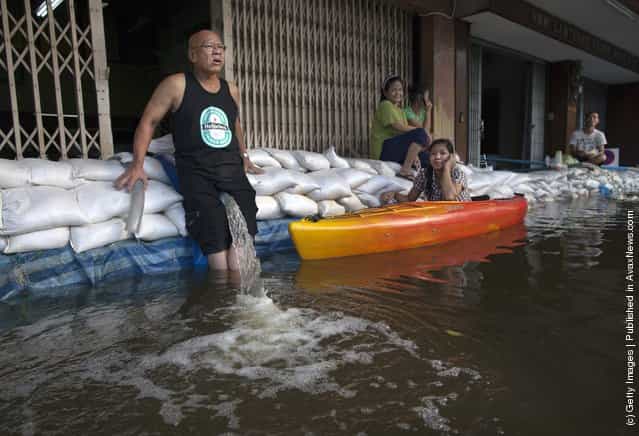 A Thai man pumps water out from his flooded home holding the hose between his legs in a neighborhood along Chao Phraya river