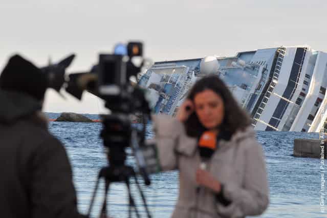 A journalist is seen in feont of the cruise ship Costa Concordia that lies stricken off the shore of the island of Giglio