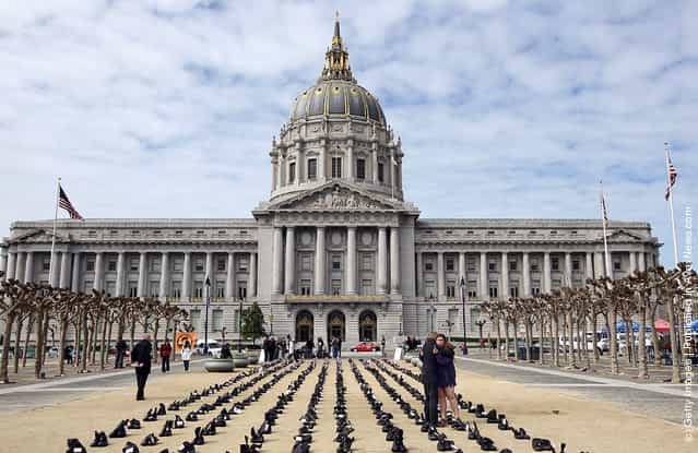 People embrace as they stand among rows of combat boots that are part of the Eyes Wide Open exhibit in front of San Francisco City Hall