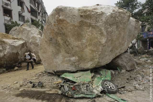 A survivor carrying goods evacuates the area past a huge rock lying on top of a car on a road near a mountain in the centre of earthquake-hit Beichuan county, Sichuan province, May 16, 2008