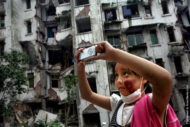 Nine-year-old Xia Xueyin, her face badly bruised during the earthquake, takes photos of her family’s damaged home in Hanwang town of Sichuan province May 22, 2008