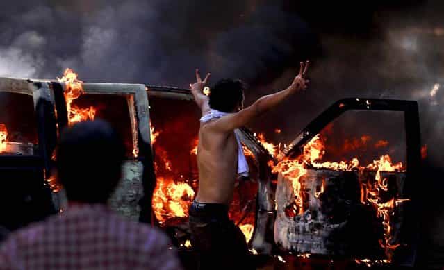 A protester flashes the victory sign next to a burning police car during clashes near the U.S. embassy in Cairo, where potesters clashed with police for the third day in a row. Egypt's Islamist President Mohammed Morsi vowed to protect foreign embassies in Cairo, where police were using tear gas to disperse protesters at the U.S. mission. (Photo by Khalil Hamra/Associated Press)