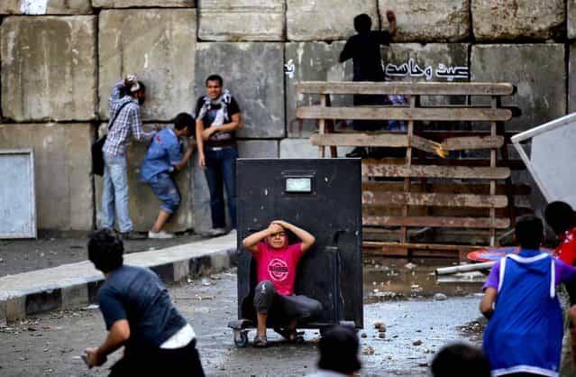 An injured protester takes cover behind a metal barrier during clashes with riot police behind cement blocks that are used to close the street leading to the U.S. Embassy in Cairo, Egypt. (Photo by Nasser NasserAssociated Press)