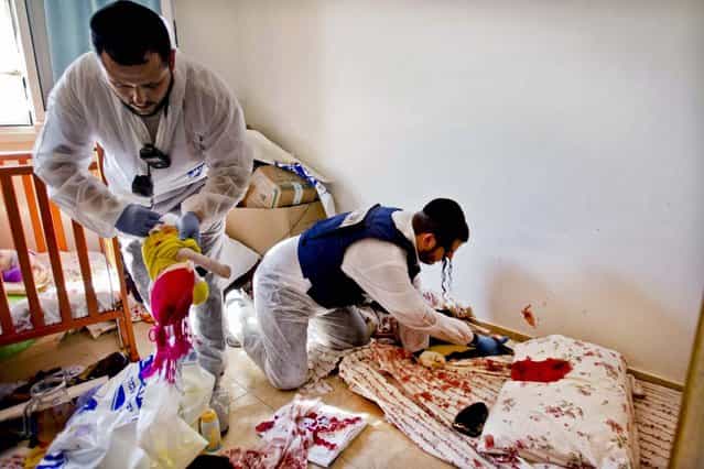 Zaka volunteers clean blood stains from a pillow and a baby toy in a children's room in an apartment building in Kiryat Malachi. (Photo by Ariel Schalit/Associated Press)