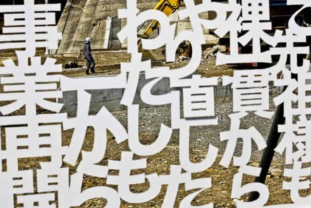 A worker walks behind a white plastic plate cutout of the words of a local businessperson, declaring determination to reopen the business, in a tsunami-stricken area in Minamisanriku, Miyagi prefecture, northern Japan, Monday, March 11, 2013. Japan marked the second anniversary on Monday of a devastating earthquake and tsunami that left nearly 19,000 people dead or missing. The words mean; I will restart my business from zero like my ancestor. (Photo by Shizuo Kambayashi/AP Photo)