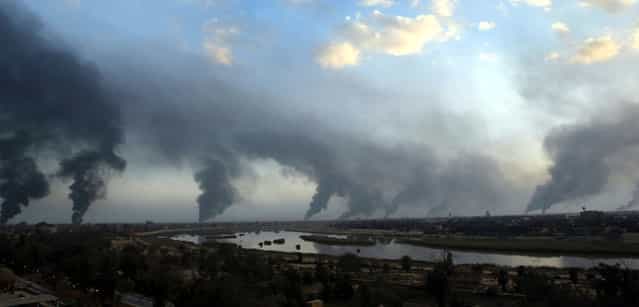 Palls of black smoke from raging oil fires billow over Baghdad, on March 27, 2003. The oil-filled trenches were set off by Iraqis to try and block the visibility of U.S. warplanes and missiles. (Photo by Goran Tomasevic/Reuters/The Atlantic)