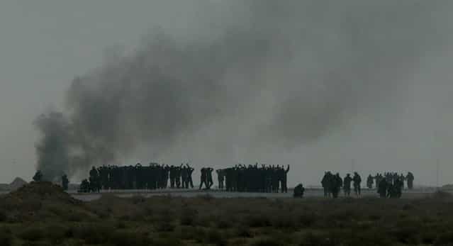 Iraqi soldiers stand together with their arms raised, silhouetted against a sky covered with black smoke as they surrender to U.S. Marines from the 15th Marine Expeditionary Unit in southern Iraq, on March 21, 2003. (Photo by Itsuo Inouye/AP Photo/The Atlantic)