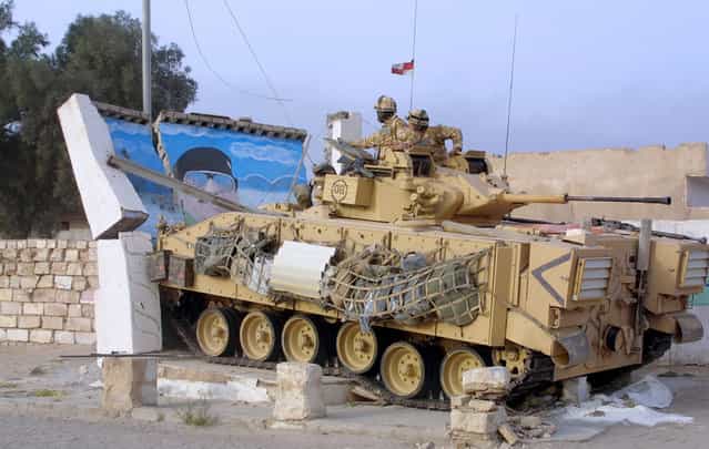 A British Warrior armored combat vehicle knocks over a picture of Saddam Hussein in the city of Basra, in southern Iraq, on March 24, 2003. (Photo by Mark Richards/Reuters/The Atlantic)