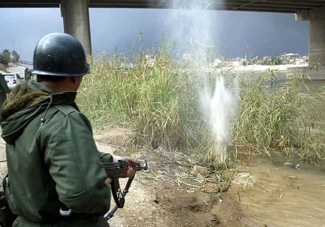 An Iraqi soldier fires his AK-47 rifle into reeds on the banks of the Tigris river in Baghdad, on March 23, 2003 after reports that U.S. or British pilots may have ejected over the city. Television reports showed Iraqi soldiers shooting into the Tigris river and in boats, apparently searching the water for pilots. (Photo by Goran Tomasevic/Reuters/The Atlantic)