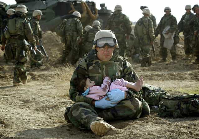 U.S. Navy Hospital Corpsman HM1 Richard Barnett, assigned to the 1st Marine Division, holds an Iraqi child in central Iraq, on March 29, 2003. Confused front line crossfire ripped apart an Iraqi family after local soldiers appeared to force civilians towards positions held by U.S. Marines. (Photo by Damir Sagolj/Reuters/The Atlantic)